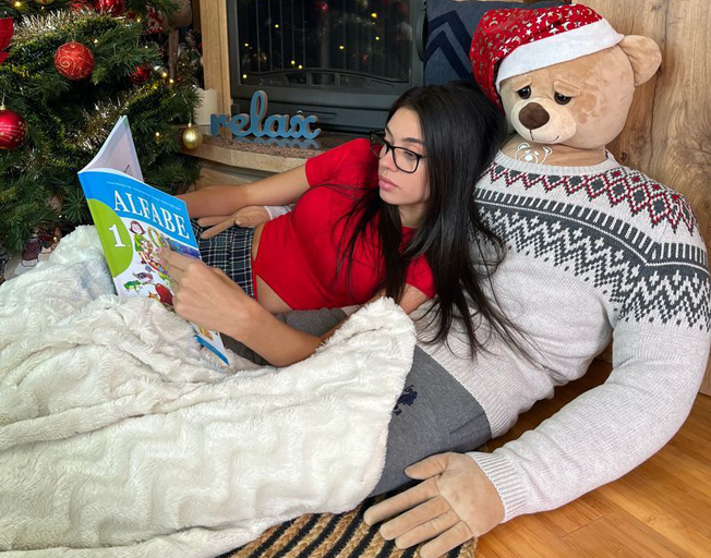 A woman reading while leaning against a man-sized teddy bear