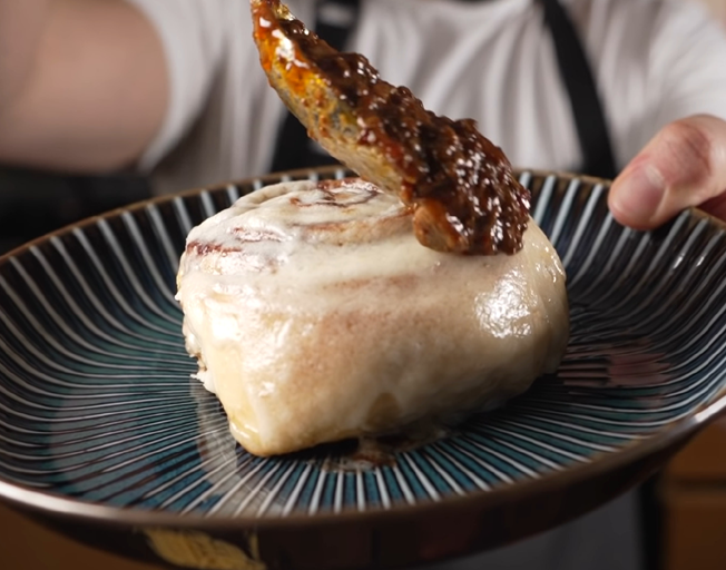 A person putting chili on a cinnamon roll